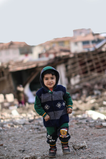 A young child standing before a city in ruins, Malatya, Türkiye