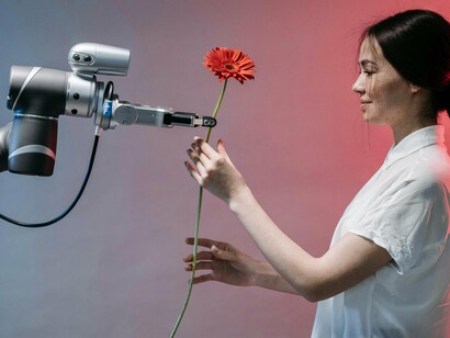 Robô oferece uma flor. A relação entre criatividade humana e IA representa uma nova etapa na produção de obras de arte. A IA, como ferramenta, amplia as capacidades de artistas, permitindo novas colaborações e expandindo os limites da criatividade tradicional