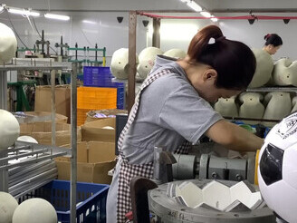 A woman is working diligently on producing footballs