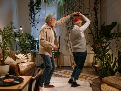 Em um momento de proximidade, um casal idoso dança e se abraça na sala de casa. As possibilidades de uma vida não se encerram nas escolhas feitas no passado: novos caminhos podem surgir em diferentes momentos da trajetória