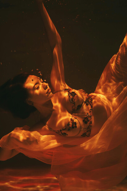 A beautiful woman underwater, wearing a brassiere and sheer skirt, captured in an artistic reflection with an abstract human profile