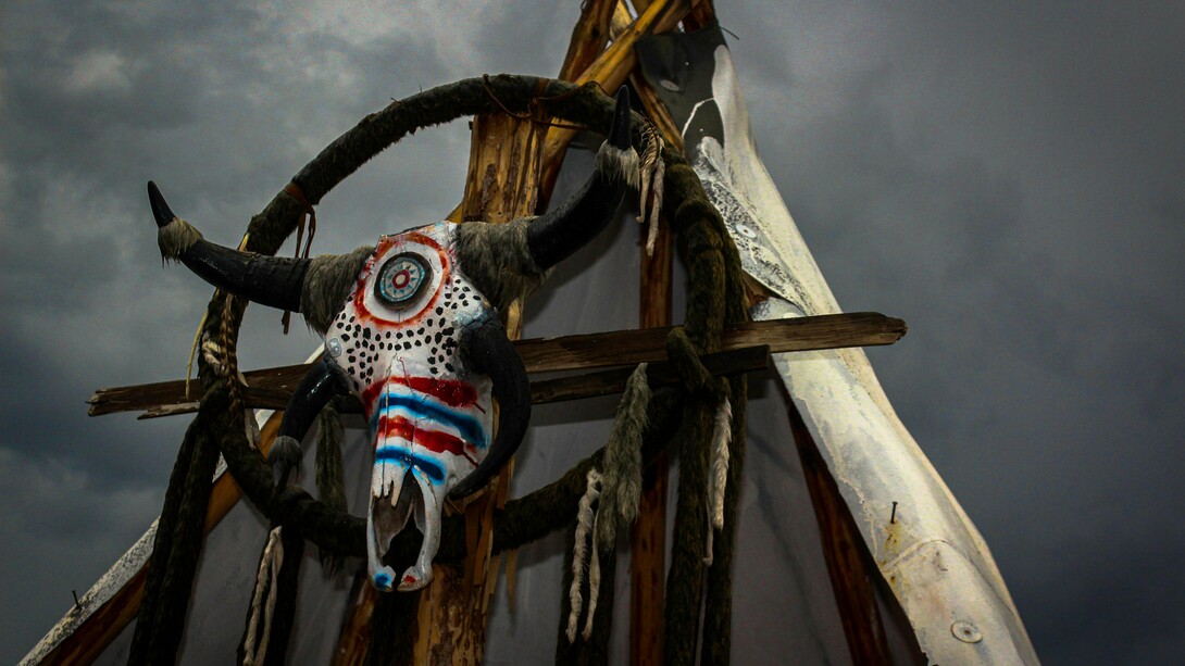 A ceremonial bull skull fixed upon a rustic wooden frame beneath a turbulent sky in Mexico, reflecting the lingering presence of ancestral belief systems