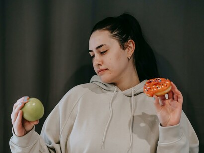 Mulher olha para a maçã enquanto segura uma rosquinha