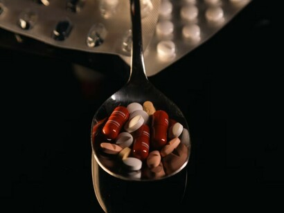A spoon loaded with an assortment of pills, resting on a table, highlighting a selection of multivitamin supplements