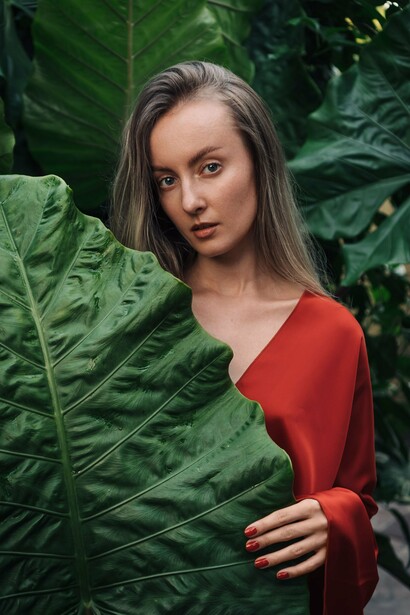 Mulher parcialmente escondida por uma grande folha tropical. A imagem sugere aquilo que permanece oculto e precisa ser reconhecido; uma ideia próxima do encontro com a própria sombra mencionado no texto
