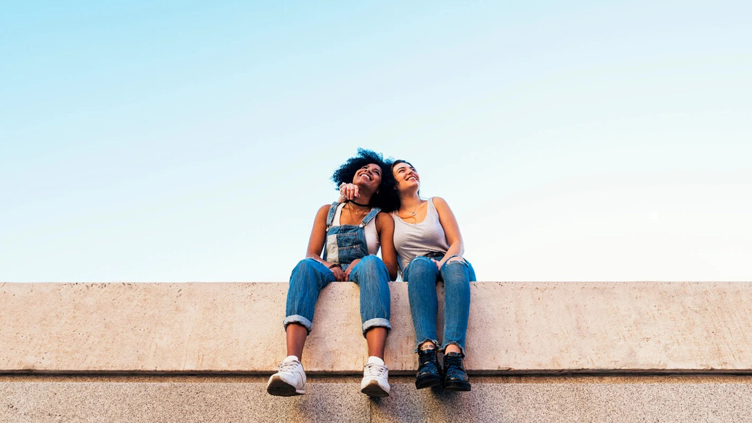 Dos amigas observan el cielo sentadas en un muro
