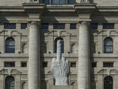 A provocação é óbvia: o dedo médio enfrenta a violência do capitalismo moderno.
A carga comunicativa da obra é particularmente impressionante porque a escultura se apresenta com uma monumentalidade triunfante: o mármore é luminoso, veias visíveis, a intenção é inequívoca.