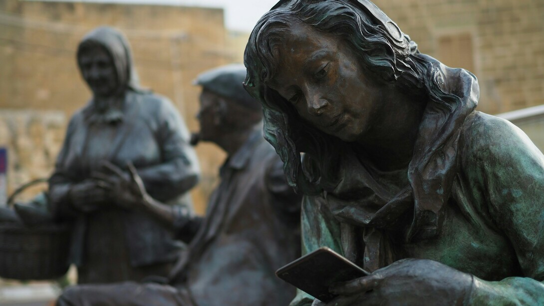 A statue of a young woman absorbed in her smartphone with headphones on, representing the quiet isolation created by constant digital immersion