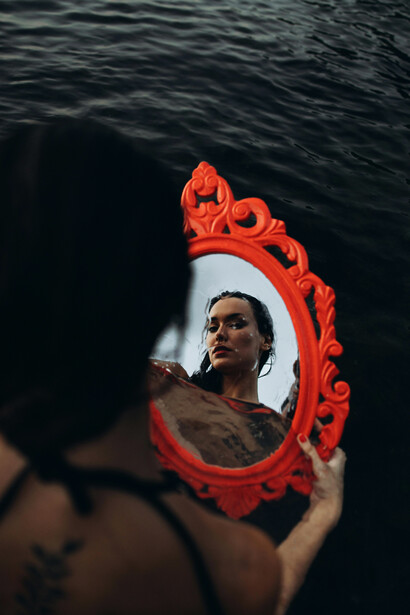 A woman in a bathing suit gazing at her reflection on the surface of the sea