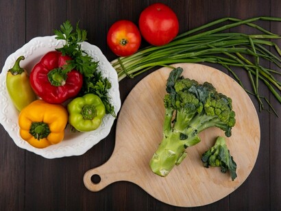 Broccoli on a cutting board, colorful bell peppers on a plate, and fresh green onions with juicy tomatoes on a rustic wooden backdrop