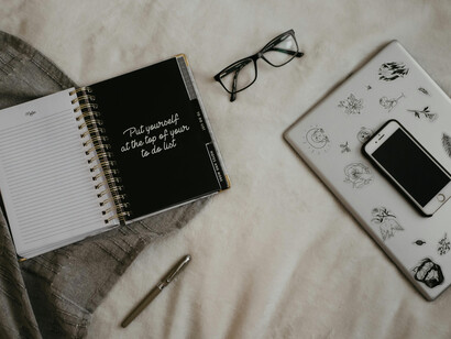 A notebook on a bed with a pen placed on top, the cover reminding with the words ‘Put yourself at the top of your to do list'