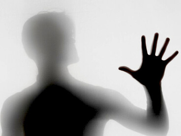 A silhouette begins to dissolve, hands reaching through shadow in a moment of transformation