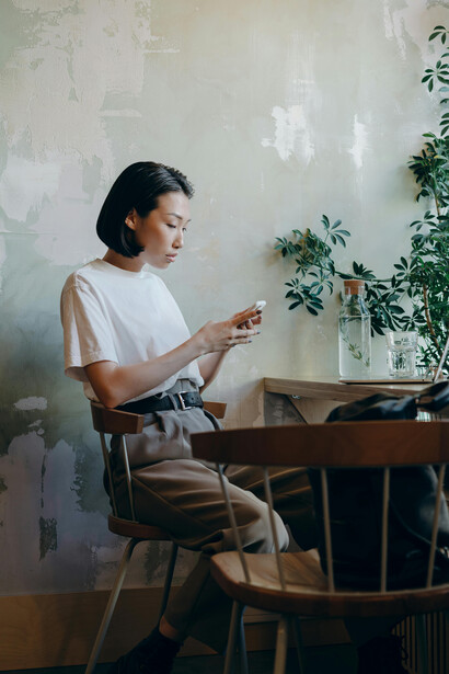 A woman in a white shirt sits alone in a cozy café, talking on the phone