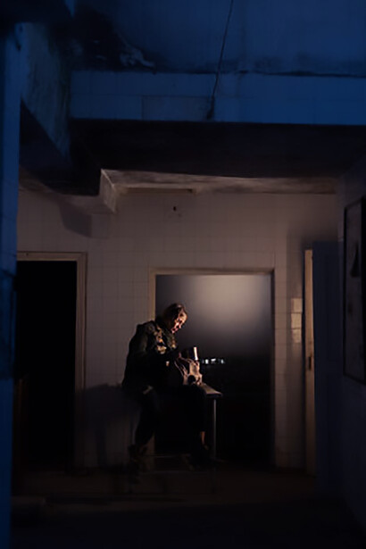 In a poignant depiction of resilience amid adversity, a solitary individual is pictured seated within an abandoned building in a war-torn area, symbolizing the struggle for survival in dire circumstances