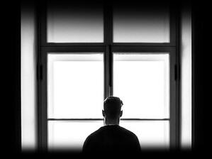 A man staring out of a window, representing loneliness brought about by social media