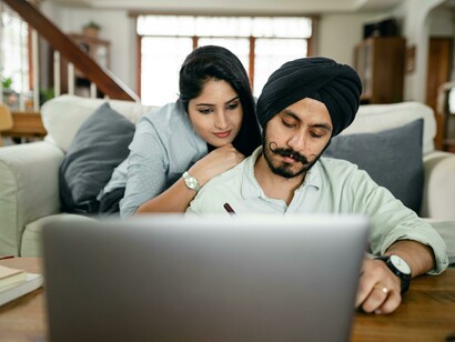 A cheerful Punjabi couple sitting together on a sofa, watching a Punjabi film from India