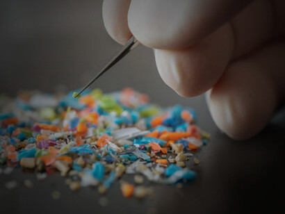 Macro shot of a person with medical gloves and tweezers inspecting a pile of micro plastics