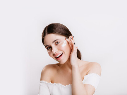A green-eyed girl smiles while applying acne treatment cream to her freshly cleansed face, focusing on her skincare routine