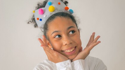 Menina negra feliz com coroa colorida com pompoms