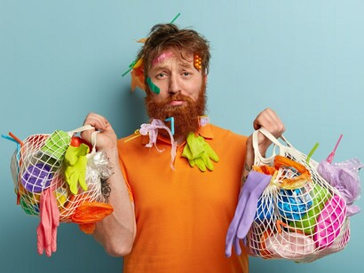 Reciclaje y contaminación plástica. Hombre descontento con cerdas gruesas, tiene basura pegada en el pelo y la barba, lleva dos bolsas llenas de basura