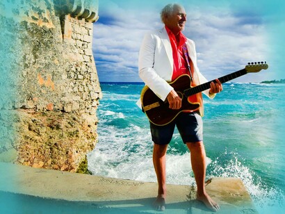 Jimmy Buffett, standing near the sea with guirtar, is best known for his laid-back, tropical-infused music, often referred to as "Gulf and Western" or "Trop Rock