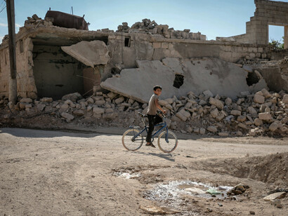 A young boy with his bicycle moves through the wreckage of a destroyed neighbourhood in Idlib, Idlib Governorate, Syria