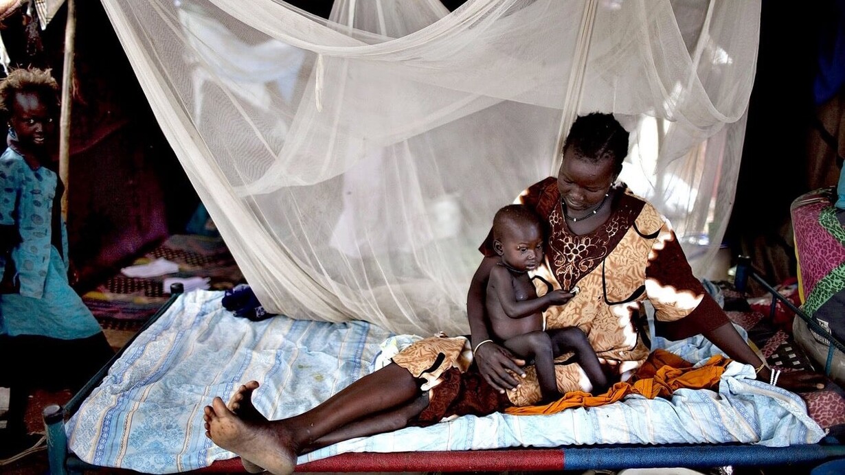 A Nilote woman laying with her baby son and her little daughter standing close by the bed, Africa