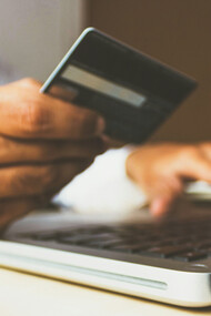 A man holding a credit card in front of his laptop