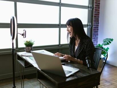 A woman in an office setting recording a video, smiling and engaging naturally with the camera