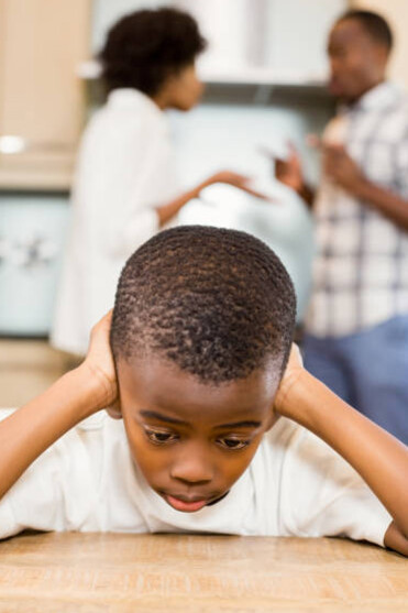 A child covers his ears at the dinner table while his parents argue
