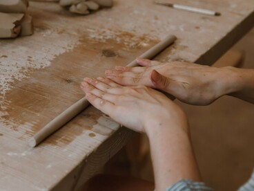 Uma pessoa trabalha a massa com as mãos sobre uma mesa, concentrando-se nos movimentos de modelagem. Assim como na cerâmica artesanal, a repetição dos gestos e o controle da pressão são fundamentais para alcançar a forma desejada