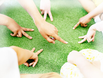 Children outside in a circle playing a game with one hand, putting two fingers in