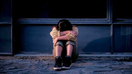 Woman sitting beside a gray wall, looking upset and depressed