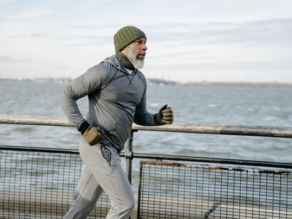 A bearded man dressed for cold jogging near a river