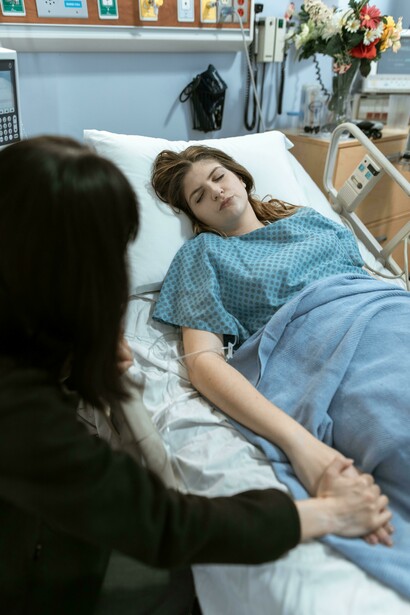 A woman gently holding a patient’s hand in a hospital, expressing warmth and compassion
