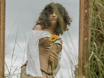 A curly haired woman looking at herself in the mirror holding a sunflower