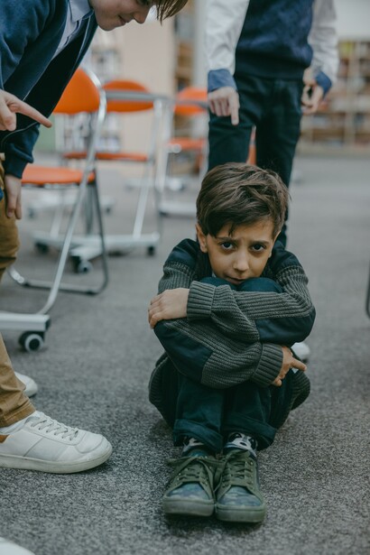 Students point finger at young boy on ground