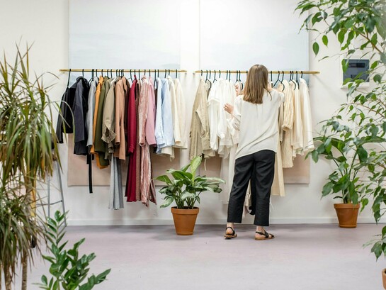 Mulher escolhe roupas em uma arara de loja. Mais do que estilo, cada escolha revela valores e um novo olhar sobre o consumo consciente. Entre peças e possibilidades, a decisão vai além da estética. Consumir moda hoje também é um ato de responsabilidade