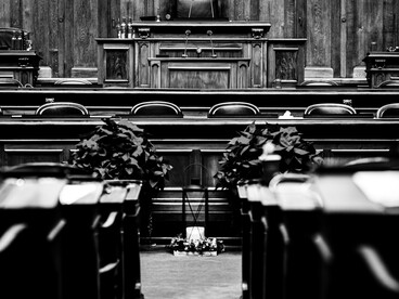 Plano en blanco y negro centrado hacia el estrado principal de una sala de debates de madera