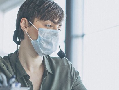 A woman in a recording studio wears a mask while working on a computer, exemplifying the digitalization trend amidst COVID-19 safety measures