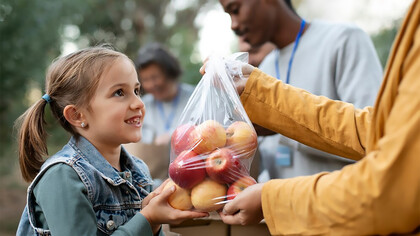 A child holding a bag of apples, offering it as a donation
