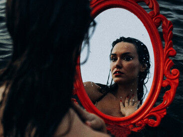 A woman in a bathing suit facing the sea as her reflection appears in the water