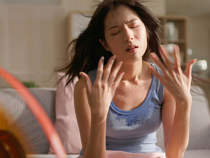 A woman experiences discomfort from the intense summer heat while resting at home
