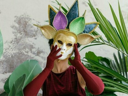 A person lifting a decorative mask to her face, symbolising the personas we wear to conceal our ordinary selves