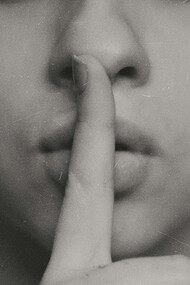 Close up of a woman's index finger pressed against her mouth, calling for quietness