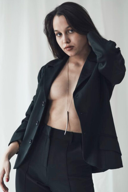 A woman strikes a bold pose in a black suit, subtly revealing she's wearing nothing beneath