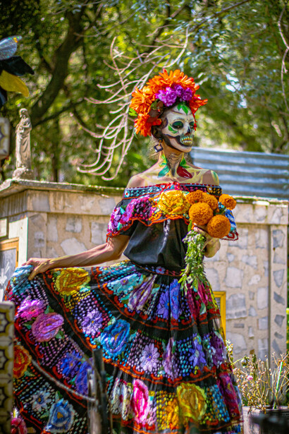 Mexico City, Mexico. A woman in colorful Catrina makeup during Día de los Muertos, standing beside a vibrant altar in the cemetery