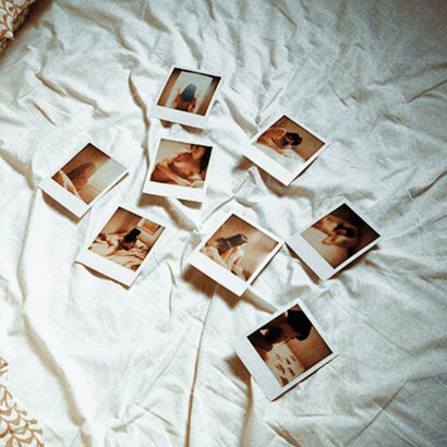 Array of suggestive polaroid images on a bed with white sheets