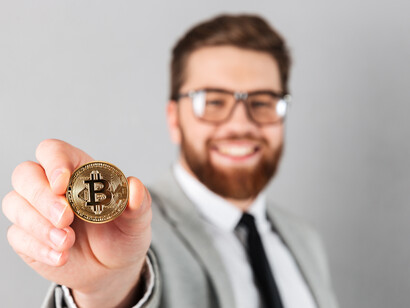 A smiling businessman in a suit holding a bitcoin, symbolizing digital currenc