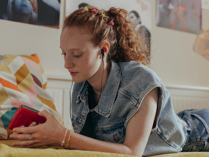 A woman in a denim vest lying down, listening to music on a Walkman